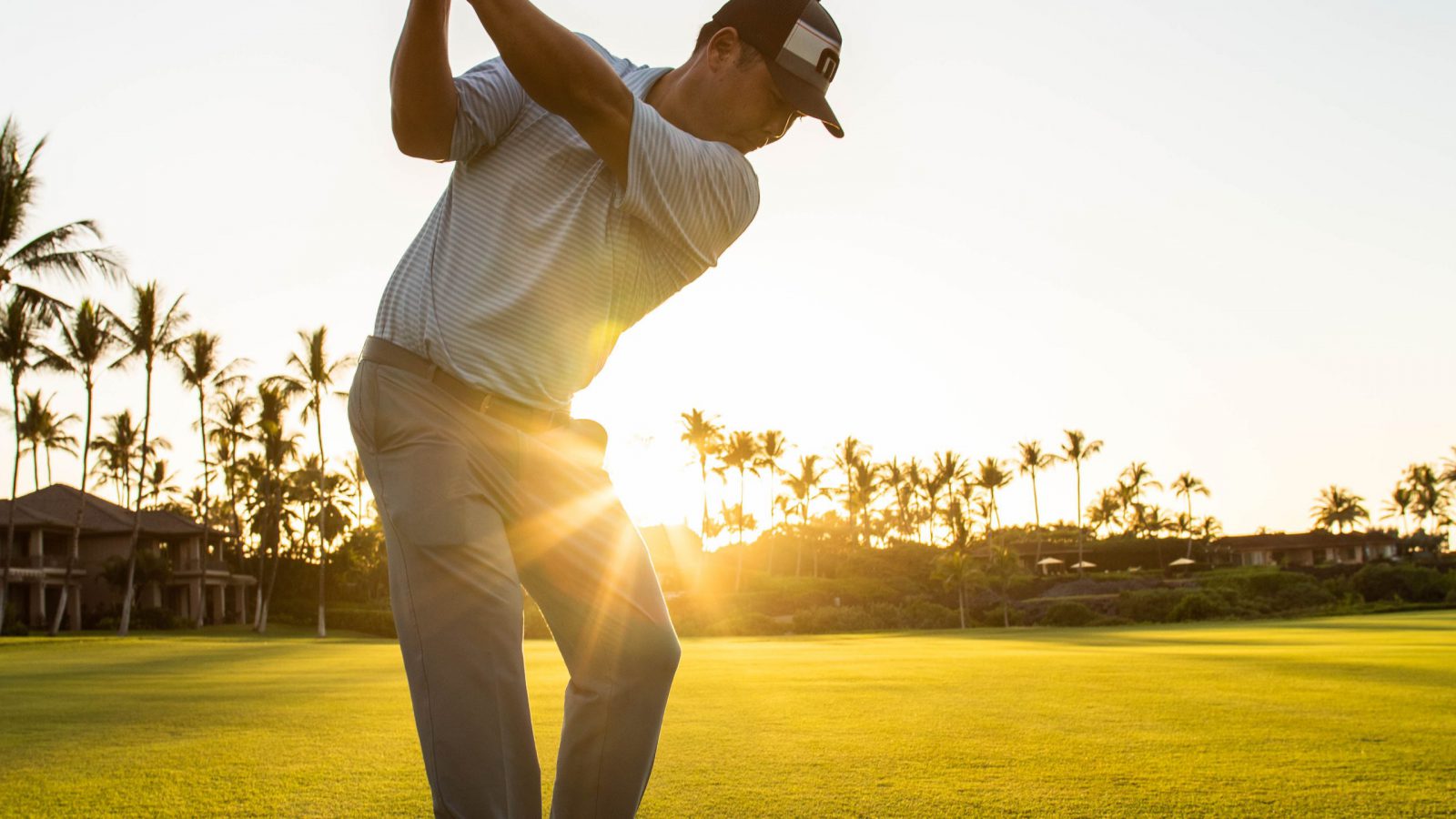 1x1 chipping clinic Golf Pro Garratt Okamura takes a swing a golf ball with setting sun in background