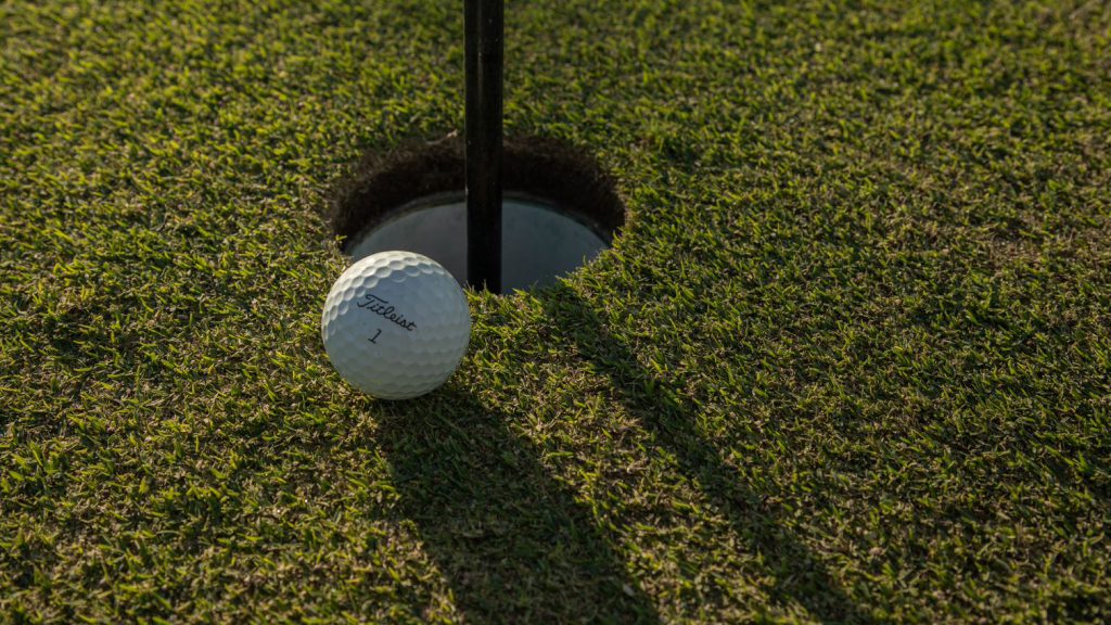 golf ball beside a golf hole with flag stick still in hole